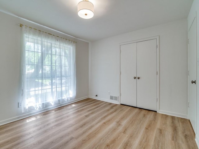 unfurnished bedroom with a closet, light wood-style floors, visible vents, and baseboards