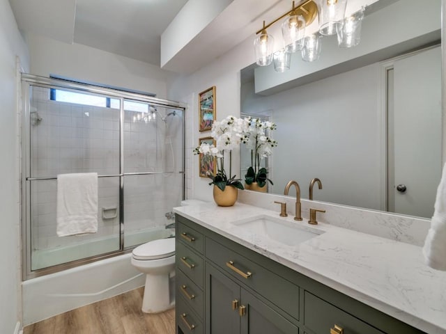 bathroom with wood finished floors, toilet, vanity, and enclosed tub / shower combo