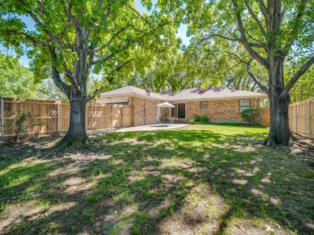 rear view of house with brick siding, an attached garage, a fenced backyard, and a patio