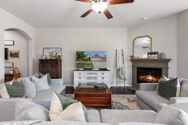 2452 Open Range Dr, Fort Worth, TX 76177 - living room featuring arched walkways, a ceiling fan, dark wood-style floors, and a lit fireplace