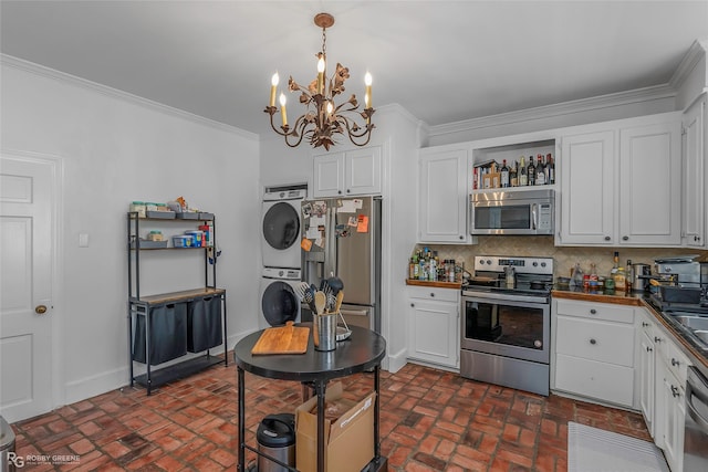 kitchen featuring appliances with stainless steel finishes, stacked washer and clothes dryer, brick floors, a chandelier, and white cabinets