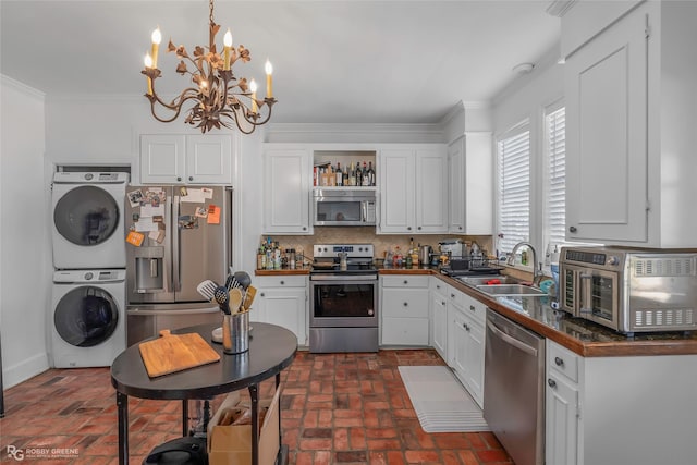 kitchen with appliances with stainless steel finishes, estacked washer and dryer, brick flooring, a sink, and a chandelier