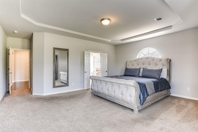 carpeted bedroom with a tray ceiling, visible vents, baseboards, and ensuite bathroom