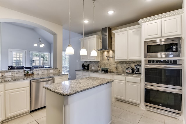 kitchen with backsplash, light tile patterned floors, a kitchen island, wall chimney exhaust hood, and appliances with stainless steel finishes