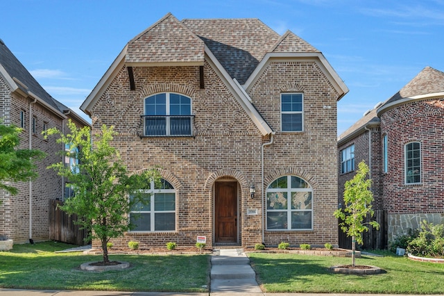 view of front facade featuring brick siding, roof with shingles, a front yard, and fence