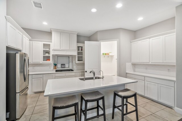 kitchen with visible vents, a sink, freestanding refrigerator, decorative backsplash, and a kitchen bar