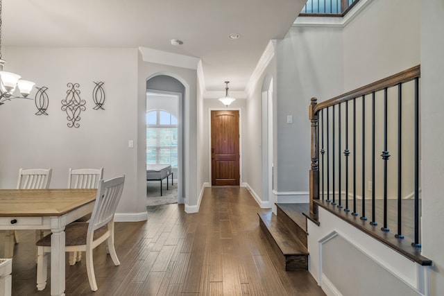 foyer featuring crown molding, a chandelier, arched walkways, baseboards, and dark wood-style flooring