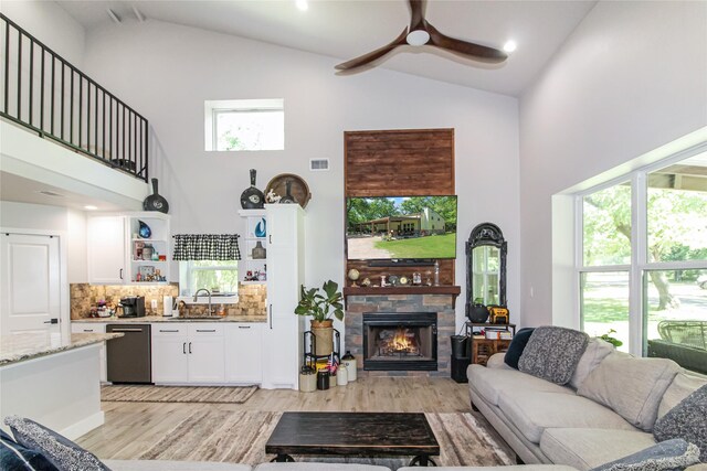 living area with a healthy amount of sunlight, light wood-style floors, ceiling fan, a stone fireplace, and high vaulted ceiling