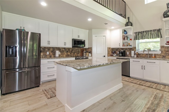 kitchen with light wood finished floors, white cabinetry, decorative backsplash, open shelves, and appliances with stainless steel finishes