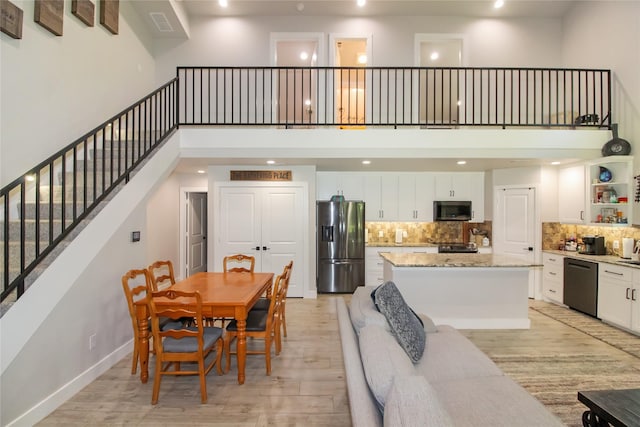 dining area featuring recessed lighting, a towering ceiling, and light wood-type flooring