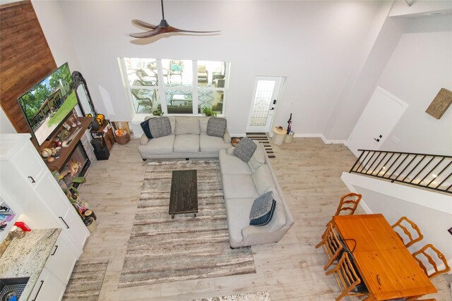 living area with a glass covered fireplace, a towering ceiling, baseboards, a ceiling fan, and wood finished floors