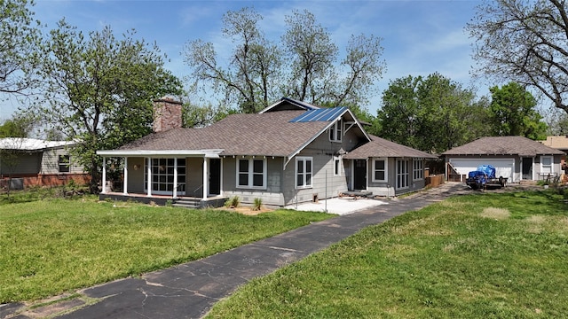 ranch-style home with a chimney, a shingled roof, a front lawn, covered porch, and a detached garage