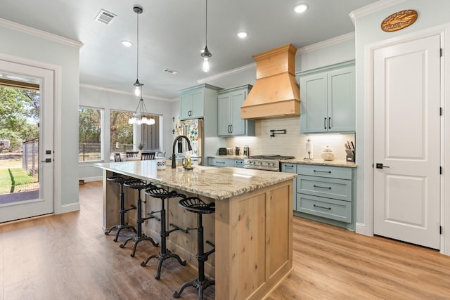 1295 County Road 2030, Glen Rose, TX 76043 - kitchen featuring custom exhaust hood, ornamental molding, light wood-style floors, a kitchen bar, and a kitchen island with sink