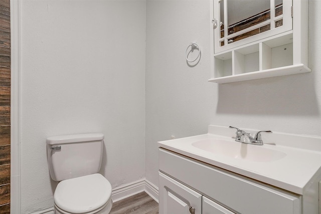 half bath featuring toilet, vanity, wood finished floors, and baseboards