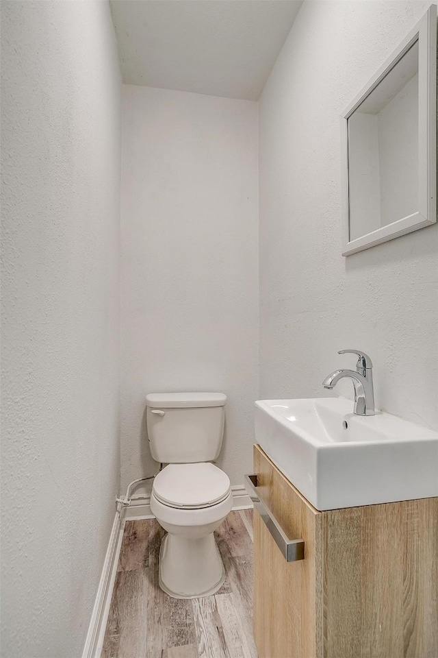 bathroom featuring wood finished floors, baseboards, vanity, and toilet