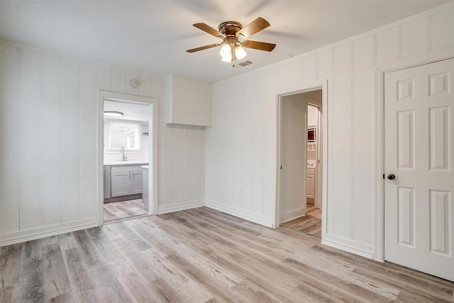 unfurnished bedroom with a decorative wall, a sink, ensuite bathroom, light wood-type flooring, and visible vents