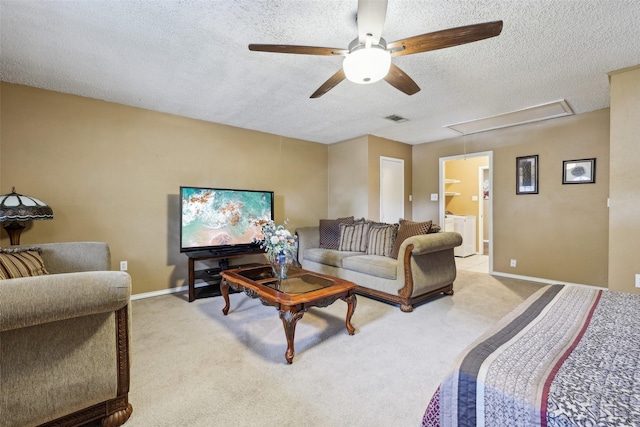 living area with a textured ceiling, washing machine and clothes dryer, visible vents, attic access, and a ceiling fan