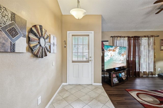 entrance foyer with light tile patterned floors, a ceiling fan, a textured ceiling, and baseboards