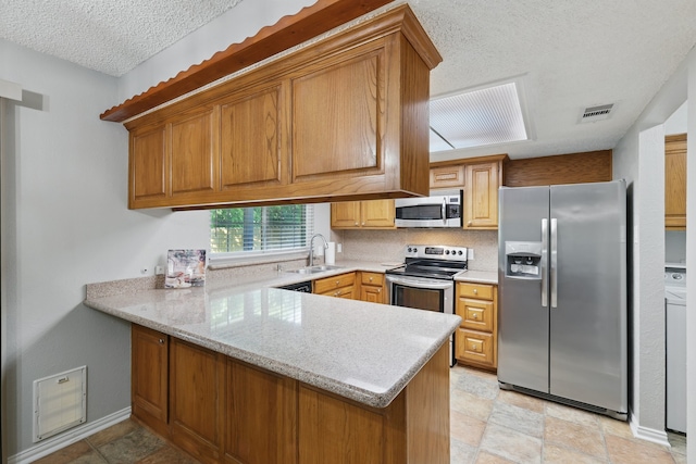 kitchen featuring a textured ceiling, a sink, stainless steel appliances, a peninsula, and visible vents