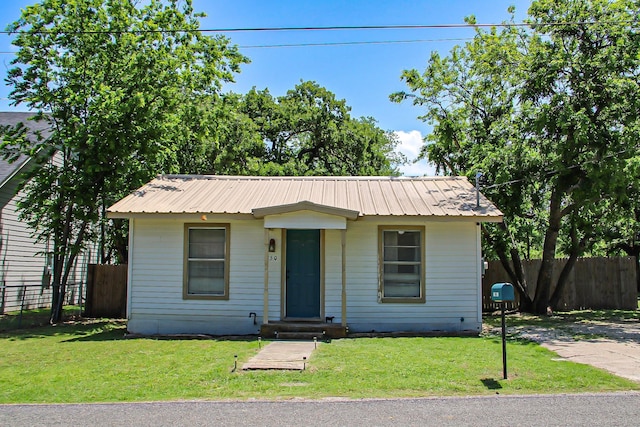 view of front facade with entry steps, a front lawn, metal roof, and fence