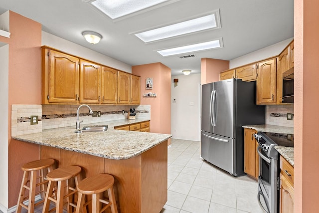 kitchen featuring stainless steel appliances, a peninsula, a sink, backsplash, and light stone counters