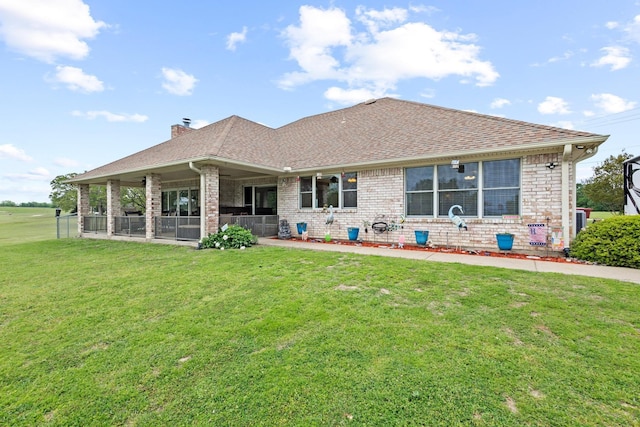 rear view of house featuring a shingled roof, brick siding, and a yard