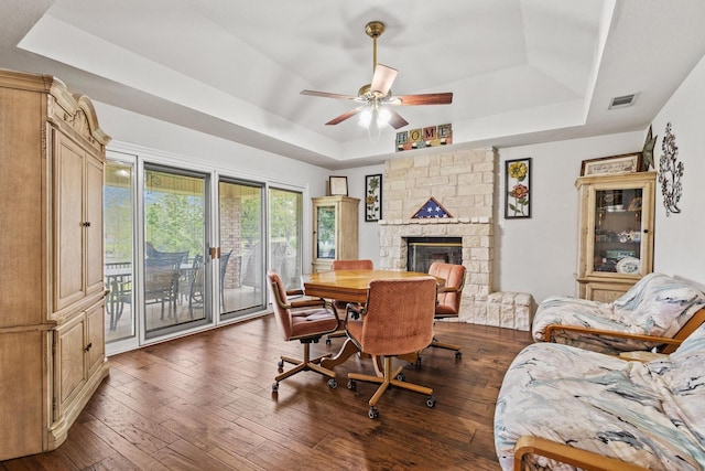 dining space with ceiling fan, a tray ceiling, visible vents, a fireplace, and dark wood-style floors