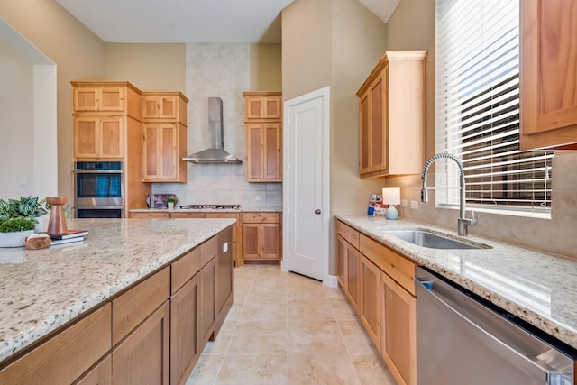 kitchen featuring wall chimney range hood, a sink, decorative backsplash, stainless steel appliances, and light stone countertops