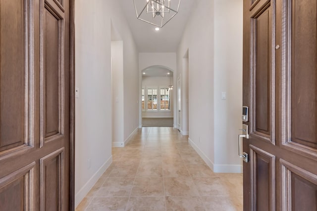 hall featuring baseboards, arched walkways, a chandelier, and light tile patterned floors