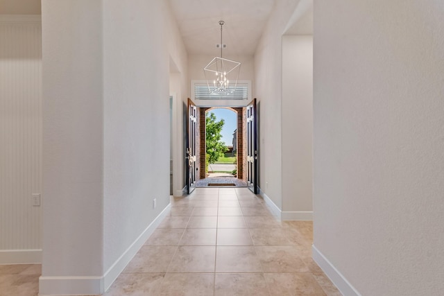 hallway with baseboards, a notable chandelier, and light tile patterned flooring