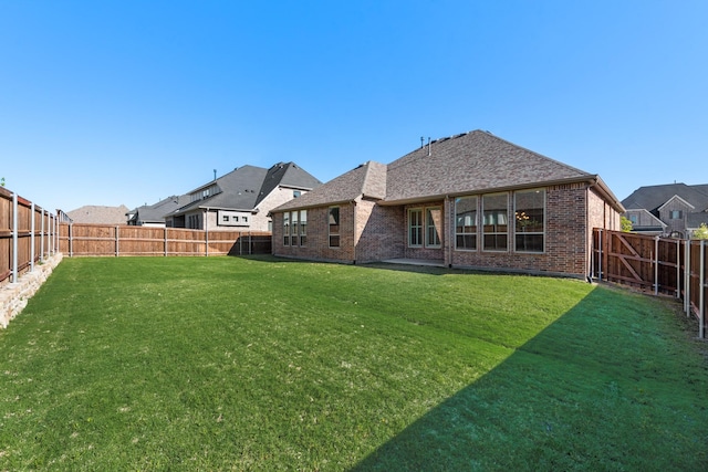 rear view of house featuring a lawn, a fenced backyard, and brick siding