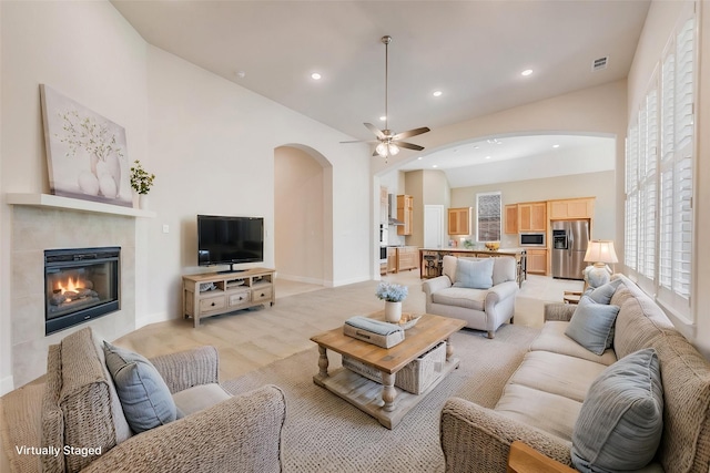 living area with a tile fireplace, arched walkways, recessed lighting, and ceiling fan
