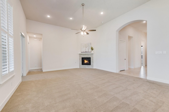 unfurnished living room with arched walkways, recessed lighting, light colored carpet, a ceiling fan, and a tile fireplace