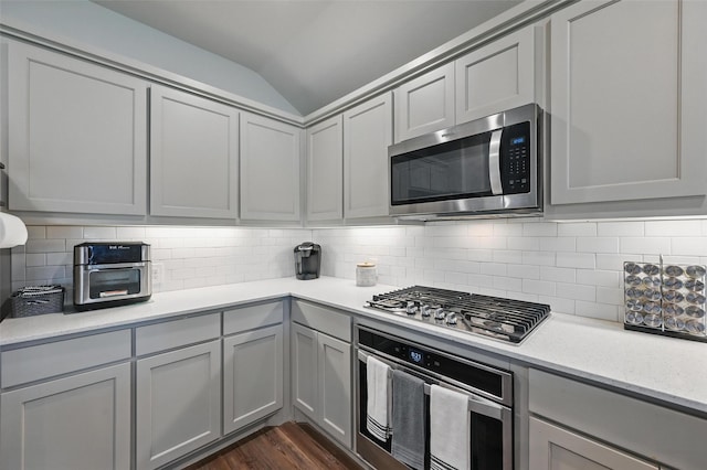 kitchen featuring decorative backsplash, stainless steel appliances, dark wood-type flooring, vaulted ceiling, and gray cabinetry