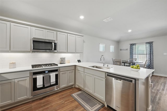 kitchen featuring a sink, a peninsula, backsplash, light countertops, and appliances with stainless steel finishes