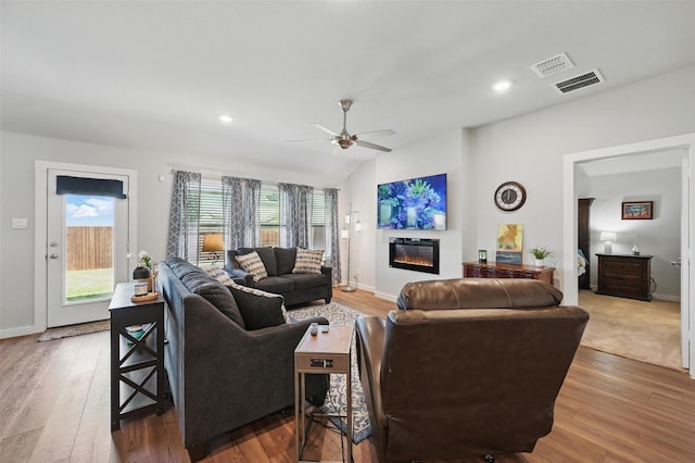 living room with a glass covered fireplace, visible vents, ceiling fan, and wood finished floors