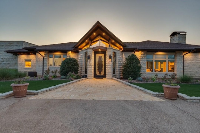 prairie-style home with a chimney, a yard, and stone siding