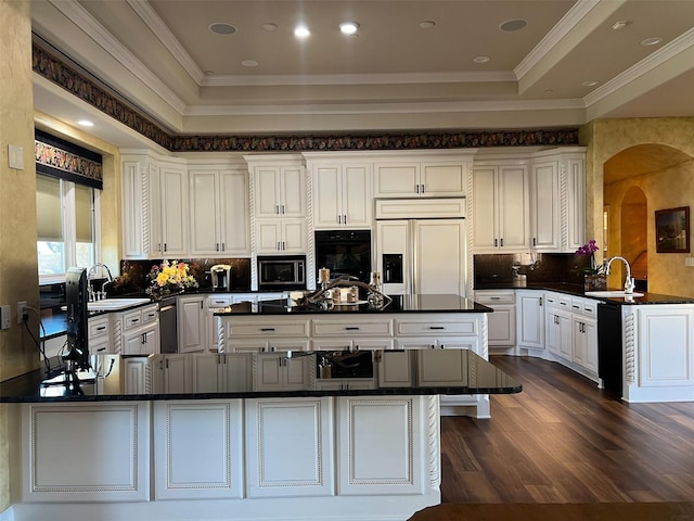 kitchen featuring black appliances, dark countertops, a peninsula, and a raised ceiling