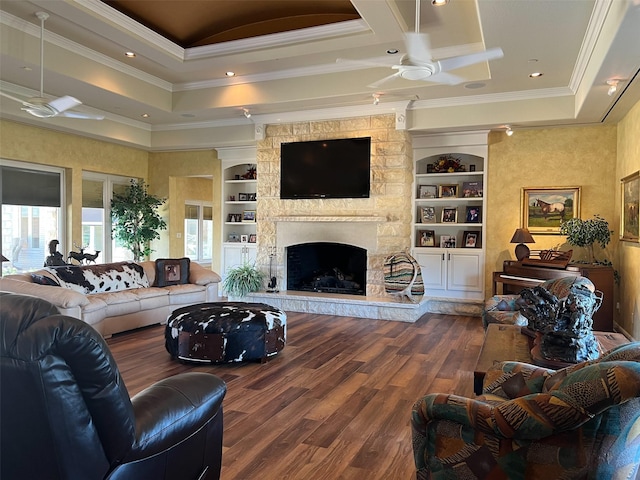 living room with wood finished floors, ornamental molding, a stone fireplace, a ceiling fan, and a tray ceiling