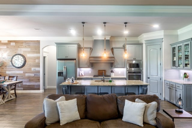 kitchen with a kitchen island with sink, open floor plan, appliances with stainless steel finishes, and premium range hood