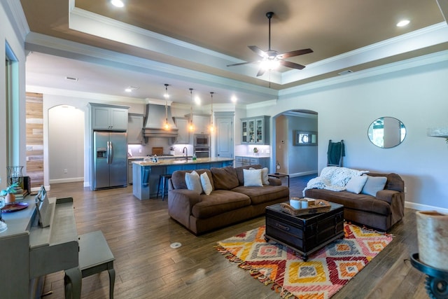 living area with ceiling fan, crown molding, arched walkways, a raised ceiling, and dark wood-style floors