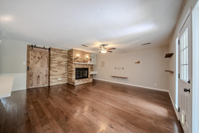 807 Eastcliff Dr, Euless, TX 76040 - unfurnished living room featuring ceiling fan, dark wood finished floors, a barn door, a textured ceiling, and a large fireplace