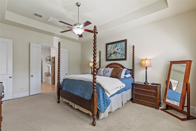 bedroom with ceiling fan, a tray ceiling, light colored carpet, baseboards, and visible vents