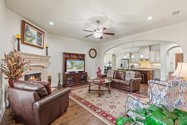 living room with dark wood-style floors, visible vents, a ceiling fan, arched walkways, and a premium fireplace
