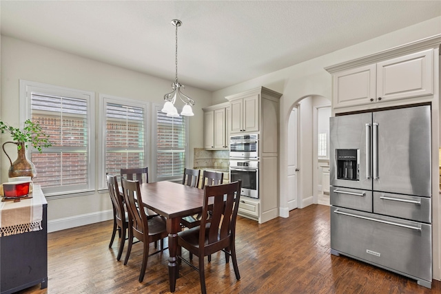 dining room with arched walkways, baseboards, and dark wood-style flooring