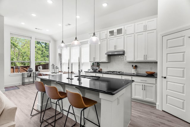 kitchen with under cabinet range hood, dark countertops, visible vents, a sink, and decorative backsplash