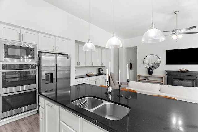 kitchen featuring dark countertops, a sink, decorative backsplash, appliances with stainless steel finishes, and open floor plan