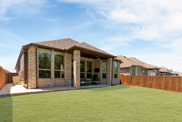 back of house with brick siding, a lawn, a fenced backyard, and a patio