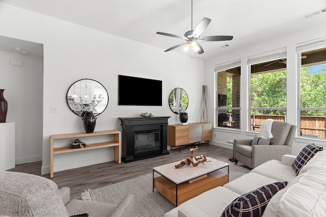 living area with baseboards, a glass covered fireplace, wood finished floors, and visible vents