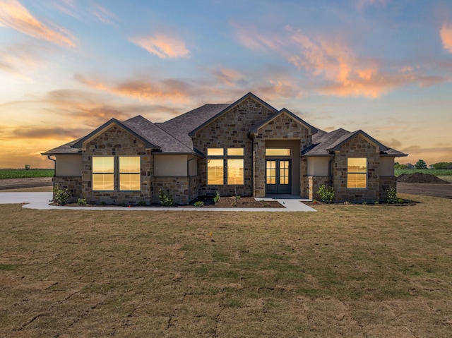 view of front of home featuring stone siding, french doors, and a yard